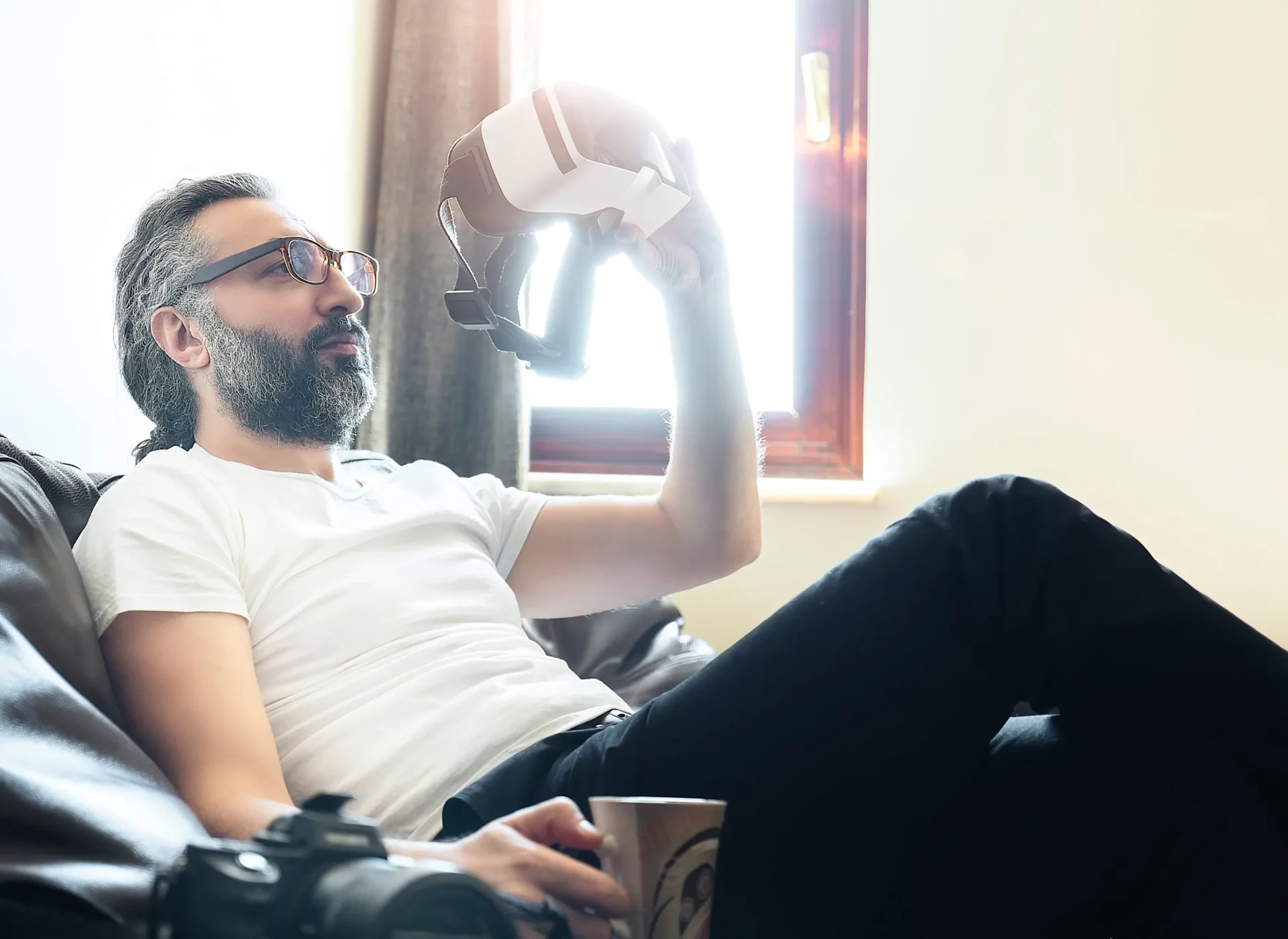 Man holding VR headset, relaxing on couch.